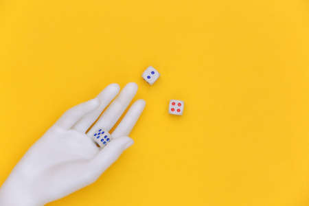 Dice in a white mannequin hand on a yellow background. top viewの写真素材