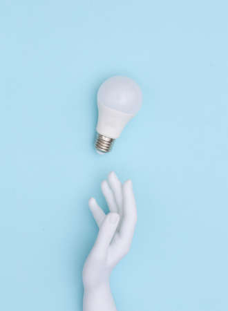 White mannequin hand and LED light bulb on blue background. top view