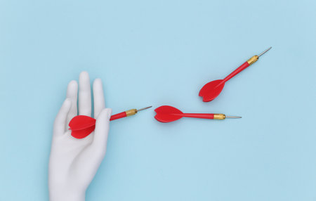 White mannequin hand holds dart needles on blue background. top view