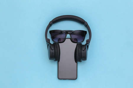 Smartphone with wireless stereo headphones and sunglasses on blue pastel background. top viewの写真素材