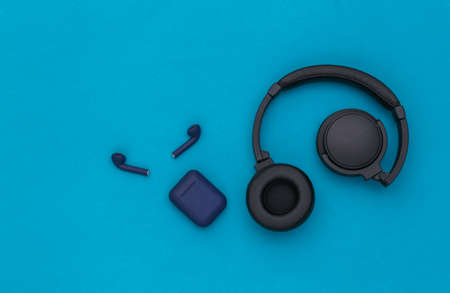 Wireless large stereo headphones and small earbuds with charger case on blue background. top viewの写真素材