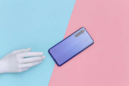 Mannequin hand and smartphone on blue-pink pastel background. Minimalism concept art. top viewの写真素材
