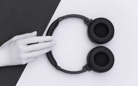 Mannequin's white hand holding stereo headphones on black white background. top view