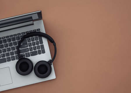 Laptop and wireless stereo headphones on a brown background. top view. copy spaceの写真素材