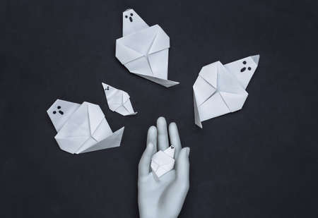 Handmade origami ghosts and mannequin hand on black background. Halloween theme. top view