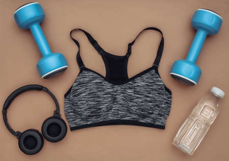 Sports top bra, dumbbells, bottle water and stereo headphones on brown background. sport and fitness. top view. flat layの写真素材