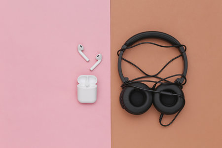 Wireless earbuds and wired tangled stereo headphones on brown pink background. top view. flat layの写真素材