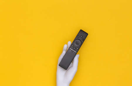 White mannequin hand holds tv remote on yellow background. top viewの写真素材