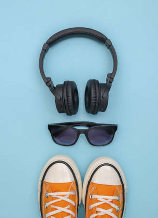 Flat lay composition of gym shoes, sunglasses and stereo headphones on a blue background. Youth accessories. top viewの写真素材