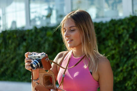 Portrait of young stylish woman with retro camera on bright sunny day outdoors