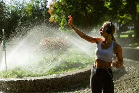 Portrait of a young slim fit woman in headphones on the background of water drops in the park at...