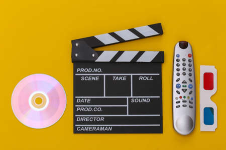 Film clapper board, 3d glasses, cd and tv remote on yellow background. top view