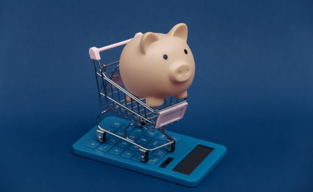 market cost. Mini shopping trolley with piggy bank and calculator on classic blue background