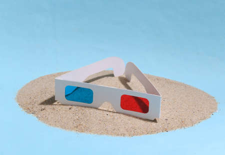 3D glasses on a sandy island. blue studio background.