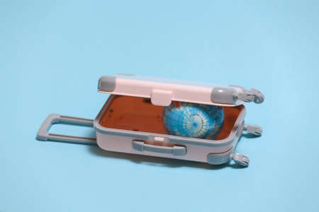 Travel or trip concept. Mini plastic travel suitcase with globe on blue background.の写真素材