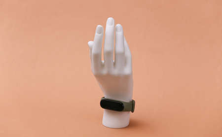 White mannequin hand stand with smart bracelet on brown background. Modern gadgets