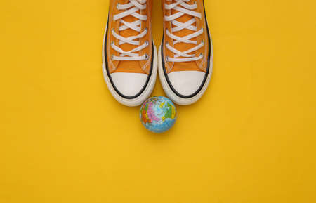 Retro sneakers (gumshoes) with globe on yellow background. travel concept. top view. copy spaceの写真素材