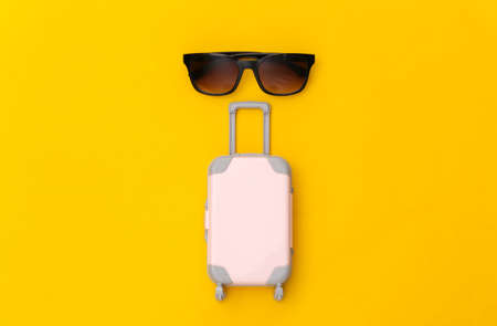Travel flat lay. Mini plastic travel suitcase and sunglasses on yellow background. minimal style. top viewの写真素材