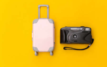 Travel flat lay. Mini plastic travel suitcase, camera on yellow background. minimal style. top viewの写真素材