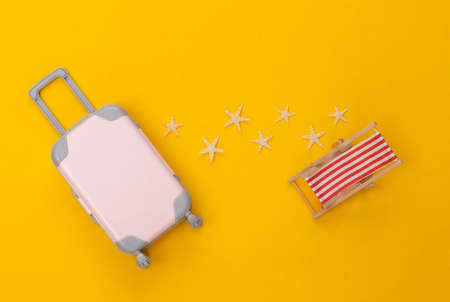 Travel or beach resort flat lay. Mini plastic travel suitcase, deck chair and starfish on yellow background. minimal style. top viewの写真素材