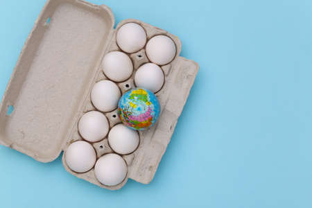 Globe in eggs tray on blue background. top view. flat lay