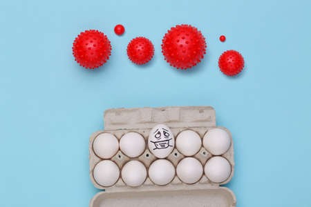The egg face with medical mask in eggs tray and virus strain on blue background. Covid-19 pandemic....