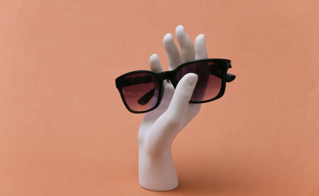 White mannequin hand holds sunglasses on brown backgroundの写真素材