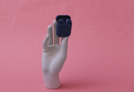 White mannequin hand holding wireless headphones with charger case on pink backgroundの写真素材