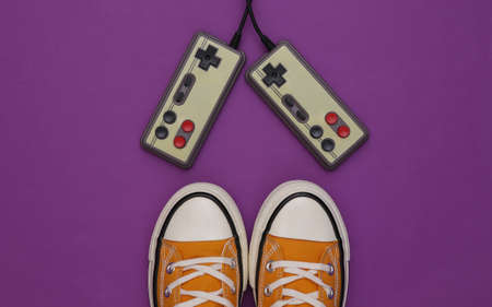 Retro sneakers (gumshoes) with retro joystick on purple background. top view. 80s. flat layの写真素材