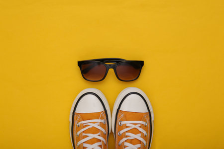 lifestyle concept. Retro sneakers (gumshoes) with sunglasses on yellow background. top view. flat layの写真素材