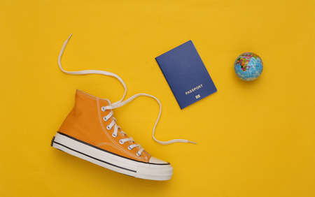 Retro sneakers (gumshoes) with globe and passport on yellow background. travel concept. top view. flat layの写真素材