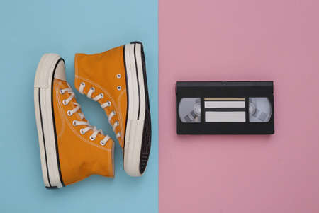 Retro sneakers (gumshoes) with video cassette on blue pink background. top view. 80s. flat layの写真素材