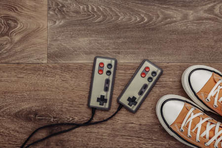 Retro sneakers (gumshoes) with retro joystick on wooden floor. top view. 80s. flat lay