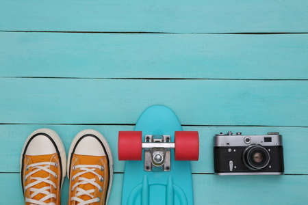 Cruiser board and gumshoes, camera on a blue wooden background. youth concept. top view. flat layの写真素材