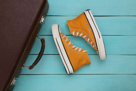 travel concept. Retro style sneakers and old travel suitcase on blue wooden background. top view