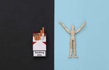 Getting rid of smoking addiction. Puppet and pack of cigarettes on blue black background