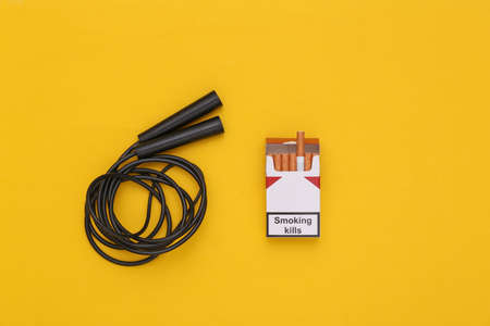 Sport or bad habits concept. Jump rope and a pack of cigarettes on yellow background. top view