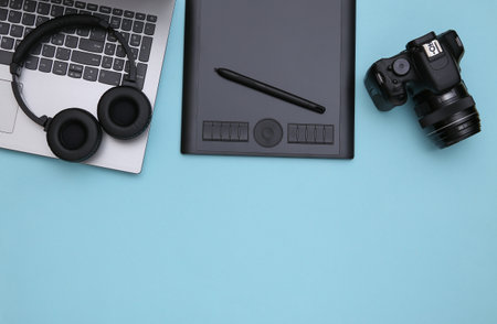 Workspace of a photographer or retoucher. Laptop, graphic tablet, camera and headphones on a blue...