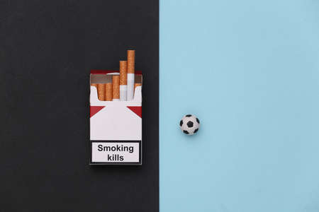 Smoking or sports. Soccer ball and pack of cigarettes on blue black background. top view