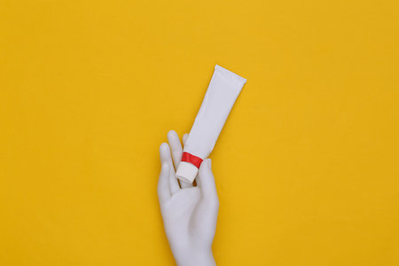 Mannequin's hand holds tube of cream or toothpaste against yellow background. top viewの写真素材