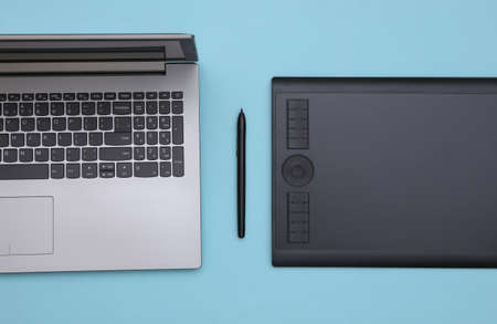 Laptop and Graphic tablet with pen on blue background. top view.
