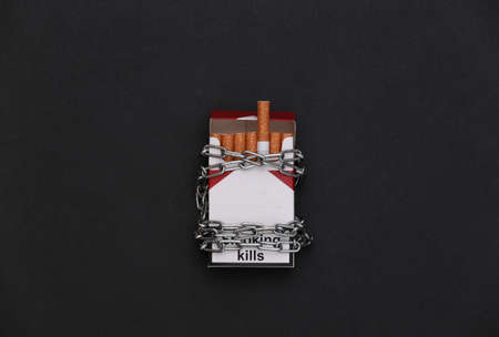 Pack of cigarettes wrapped in a steel chain on black background