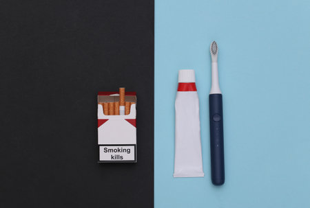 Dental care and bad habits concept. Pack of cigarettes, Tube of toothpaste with toothbrush on blue black backgroundの写真素材
