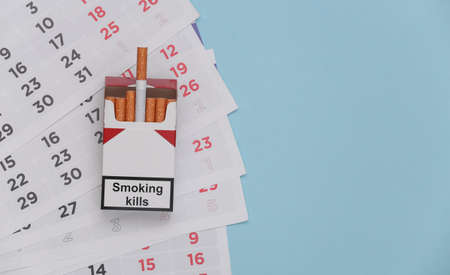 Pack of cigarettes and monthly calendar on blue background. Quitting smoking conceptの写真素材