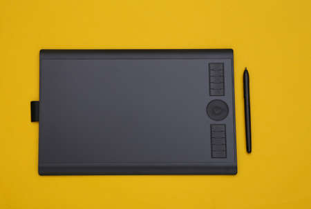 Graphic tablet with pen on yellow background. top viewの写真素材