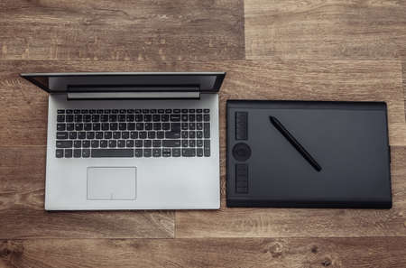 Laptop and Graphic tablet with pen on wooden background. top view.