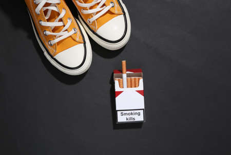Gumshoes and pack of cigarettes on black background.の写真素材