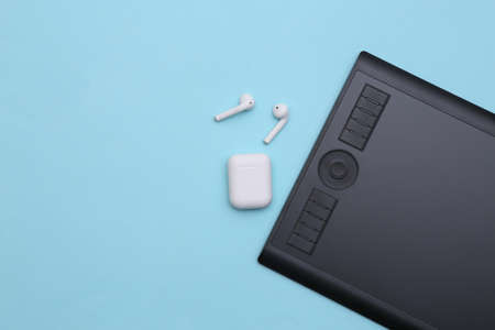 Graphic tablet with wireless headphones on blue background. top view