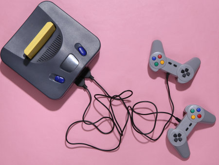 Retro video game console with joysticks on pink background. top view