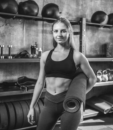 Fit woman with perfect body holds rolled mat in the gym and and posing on the cameraの写真素材